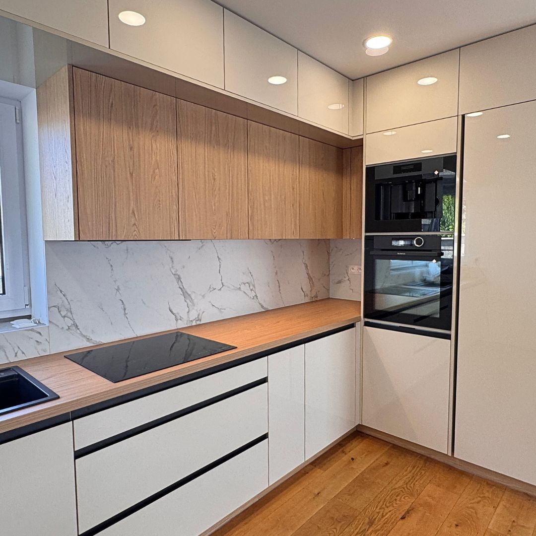 Kuchyňa vyrobená na mieru v modernom štýle – prevažne biele, vysokolesklé skrinky bez úchytiek sú zjemnené vodorovnými pásmi prírodného dubu.